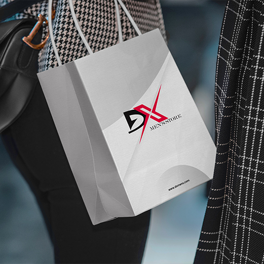 Close-up of a gray DX Men’s Store paper shopping bag with the red and black DX logo, carried by a person wearing patterned clothing. Digital Marketer