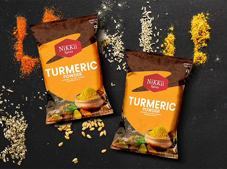 On a dark background with turmeric, grains, and spices strewn about, two packets of NiKKii Spices Turmeric Powder are displayed. Digital Marketer