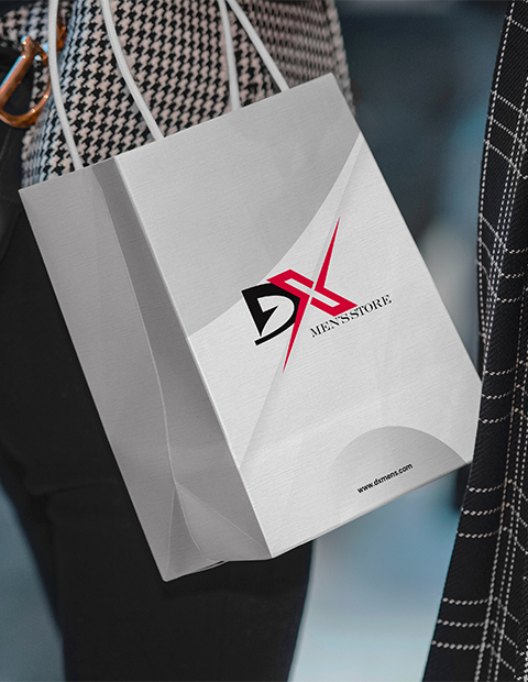 Close-up of a gray DX Men’s Store paper shopping bag with the red and black DX logo, carried by a person wearing patterned clothing. Digital Marketer